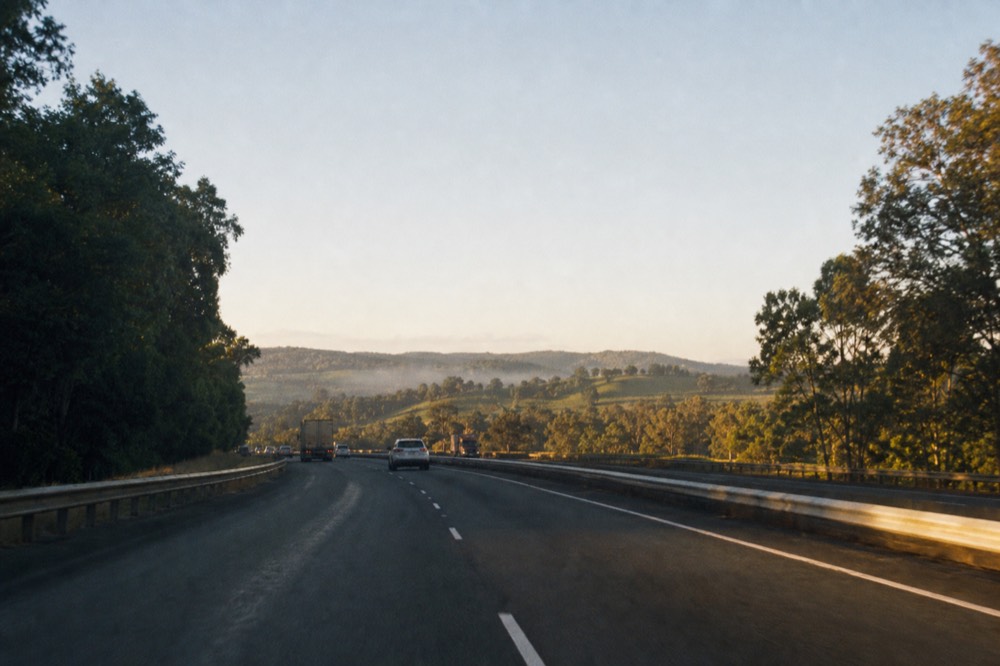 An early freeway heading toward green hills with light morning traffic, soft sunrise light, no text, no logos, no people