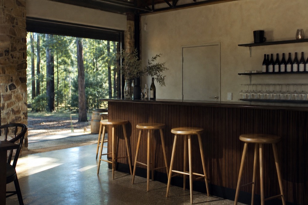 Casual tasting counter with a few empty stools and bottles on a shelf behind, soft afternoon light, no text, no logos, no faces
