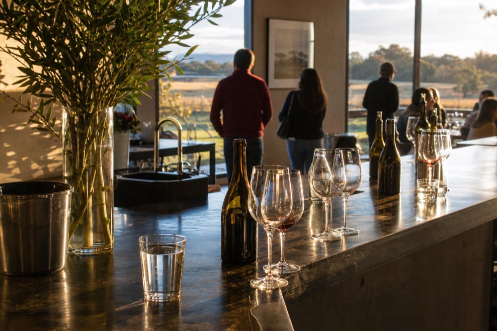 A casual stand-up tasting bar with guests' glasses and bottles along a polished counter, bright room, no text, no logos, no people
