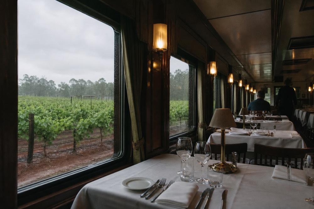 Interior of a restored dining rail car with white-clothed tables and large windows framing vineyard rows, warm light, no text, no logos, no people